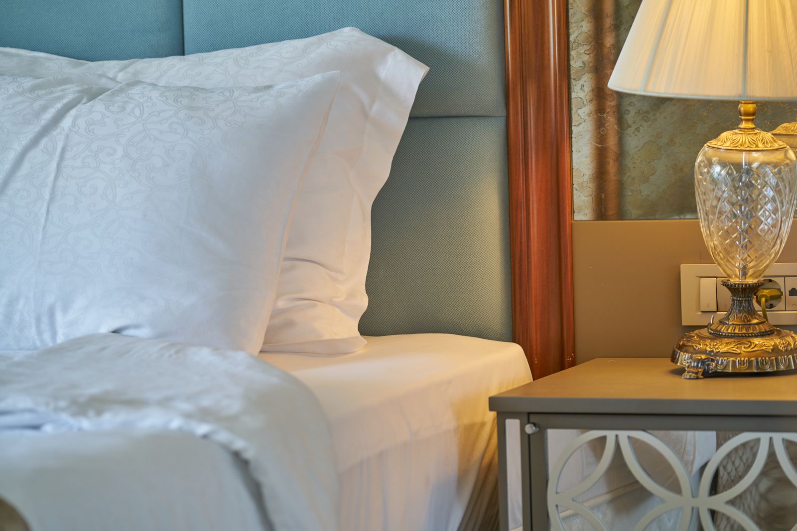 A dressed hotel bed beside a crystal lamp